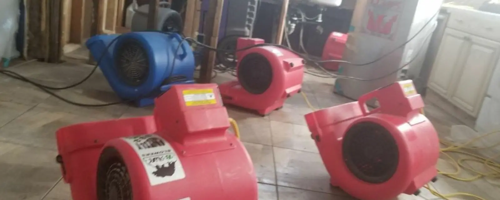 Row of red air movers drying a tile floor beside an opened wall
