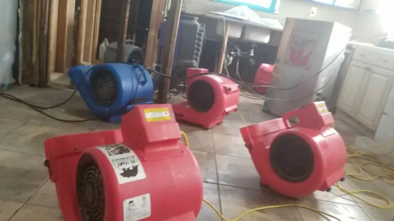 Row of red air movers drying a tile floor beside an opened wall